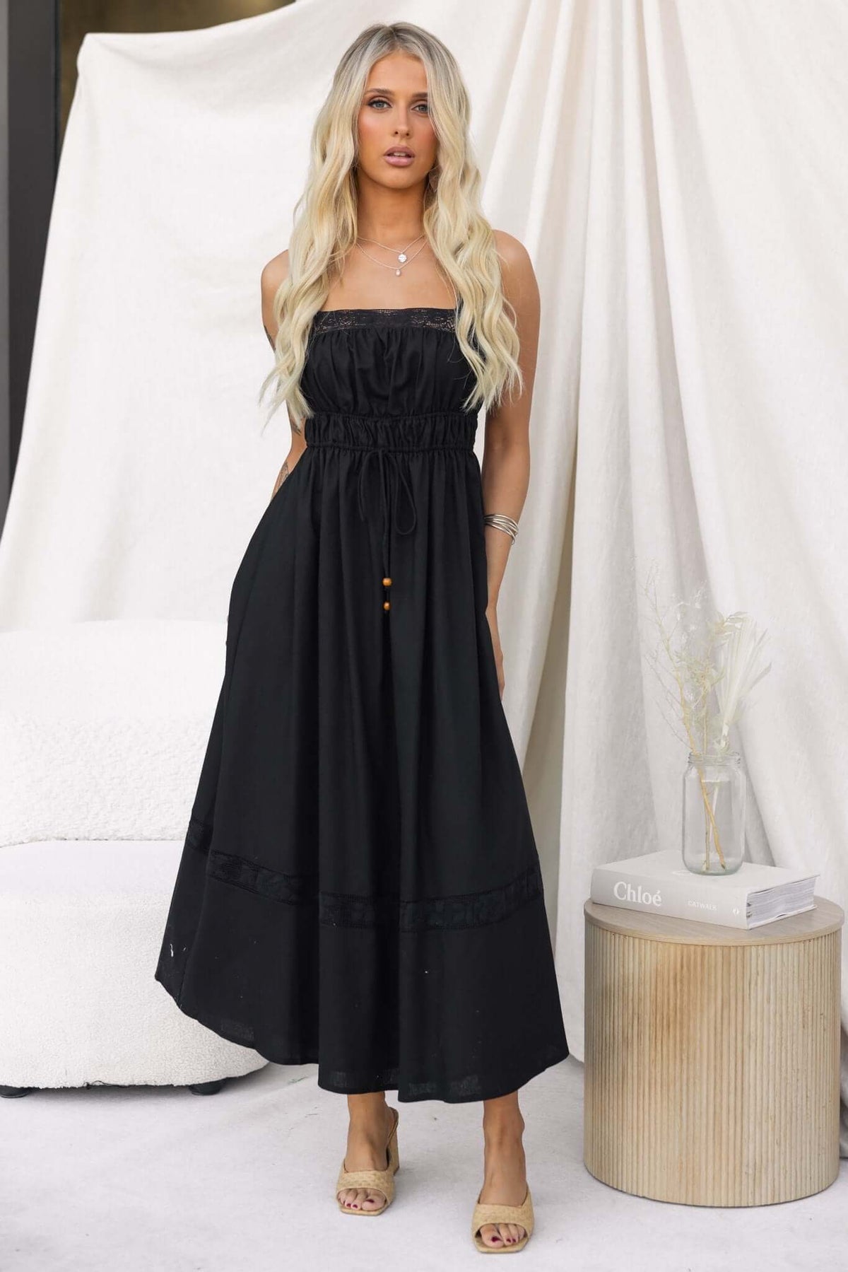 Eletti Midi Dress in black featuring lace detailing, elastic waist, and side zip, styled with a natural backdrop.