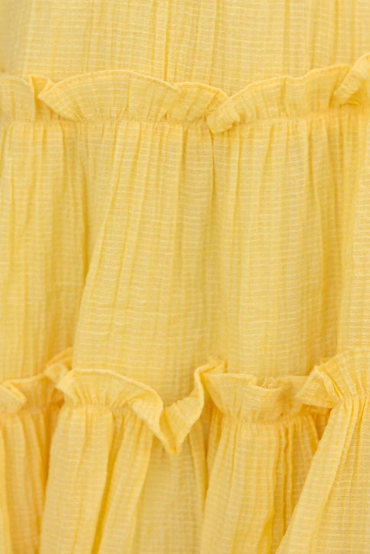 Close-up of a textured yellow dress fabric featuring ruffled seams and a lightweight, airy design.