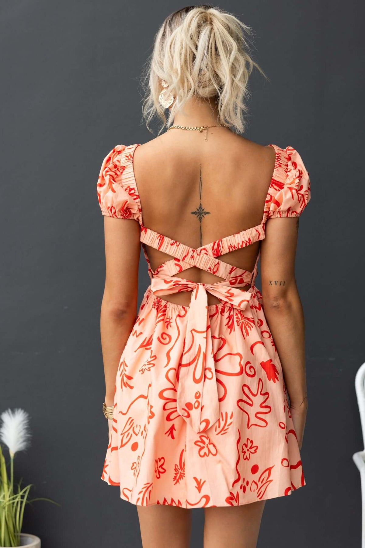 Back view of Missie Dress featuring puff sleeves, tie detail, and floral print in soft coral tones.