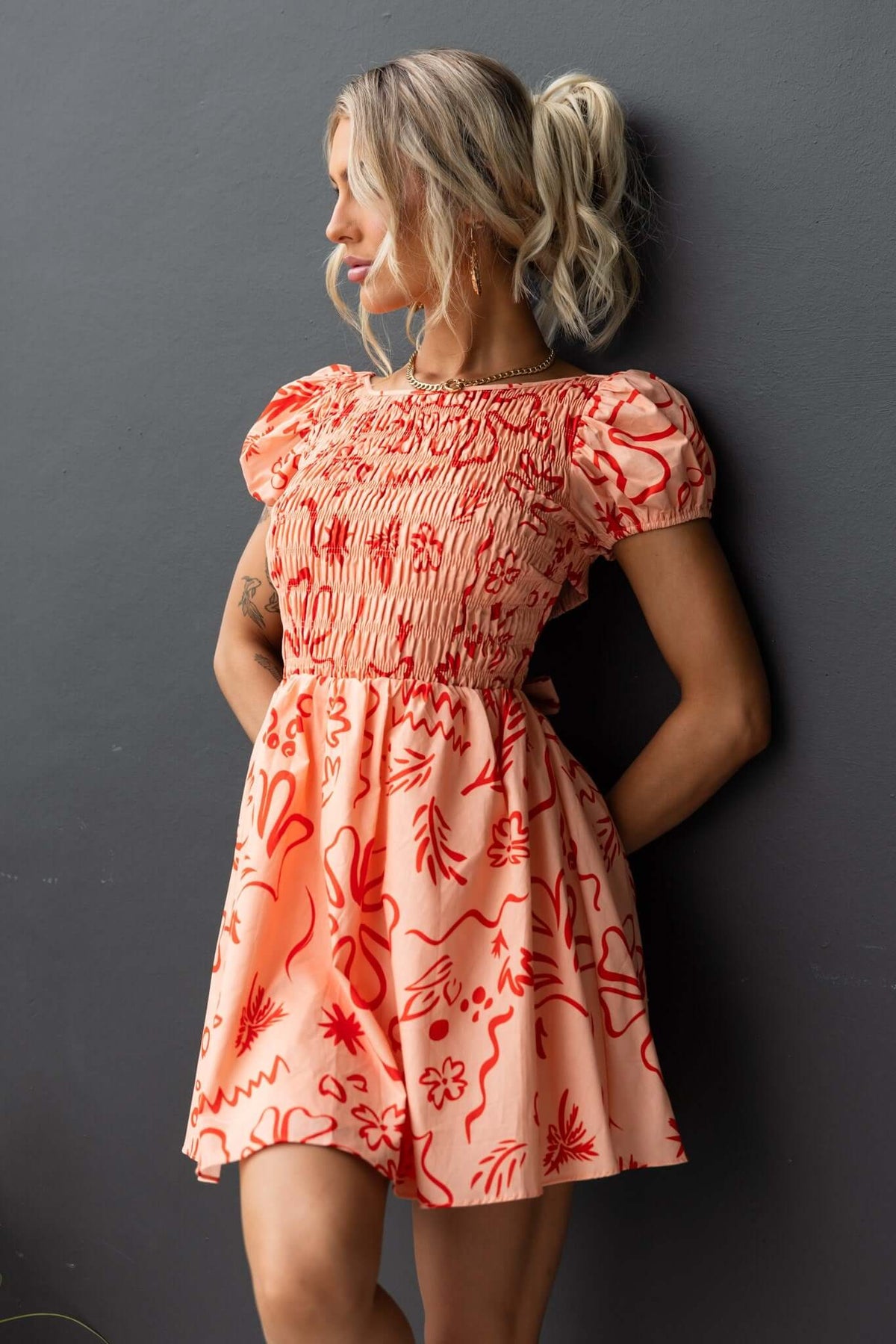 Missie Dress in coral with floral print, featuring an elastic bodice, puff sleeves, and a fitted waist.