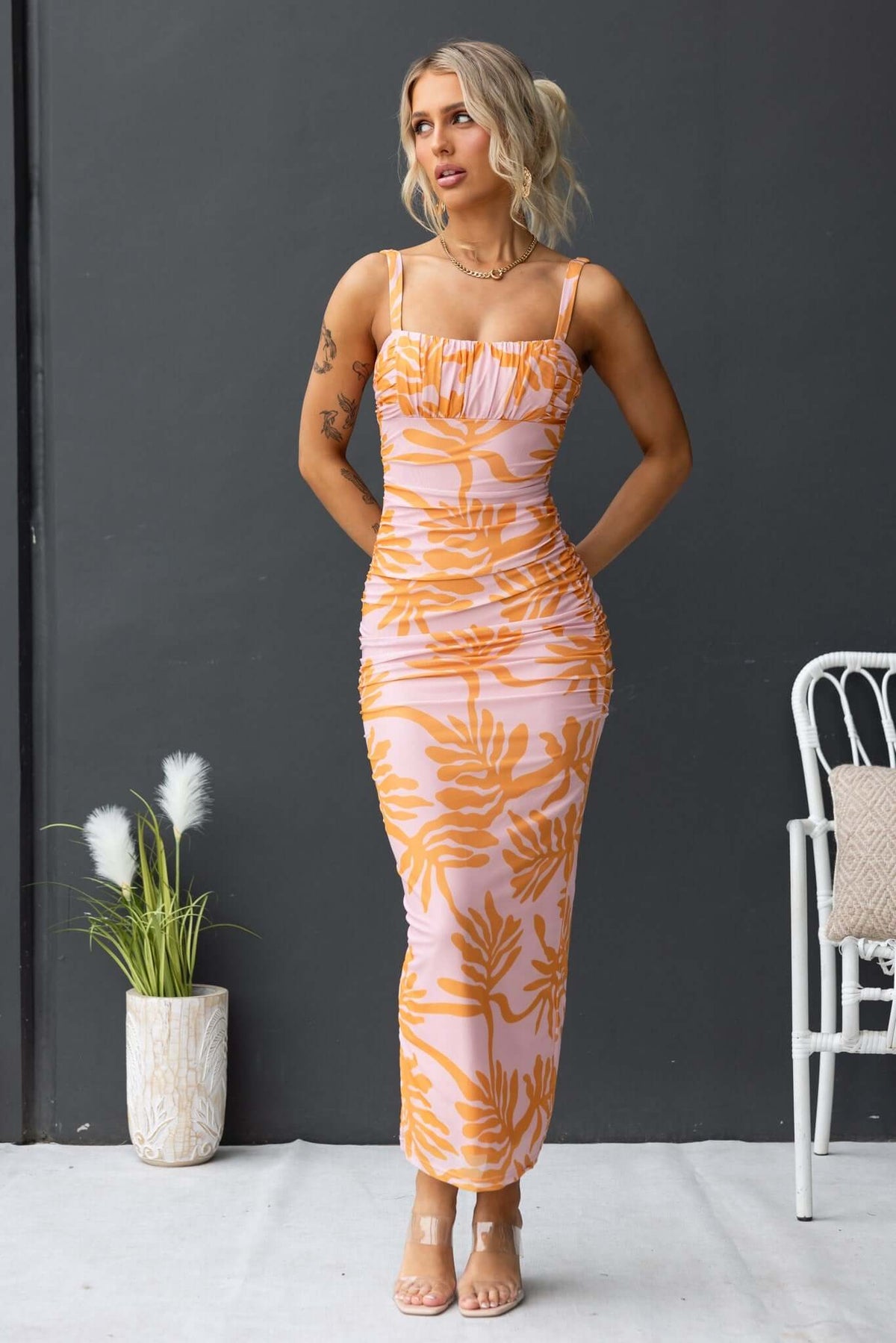 Giorgi Maxi Dress featuring floral print, adjustable straps, and ruching, modeled by a woman with a plant background.