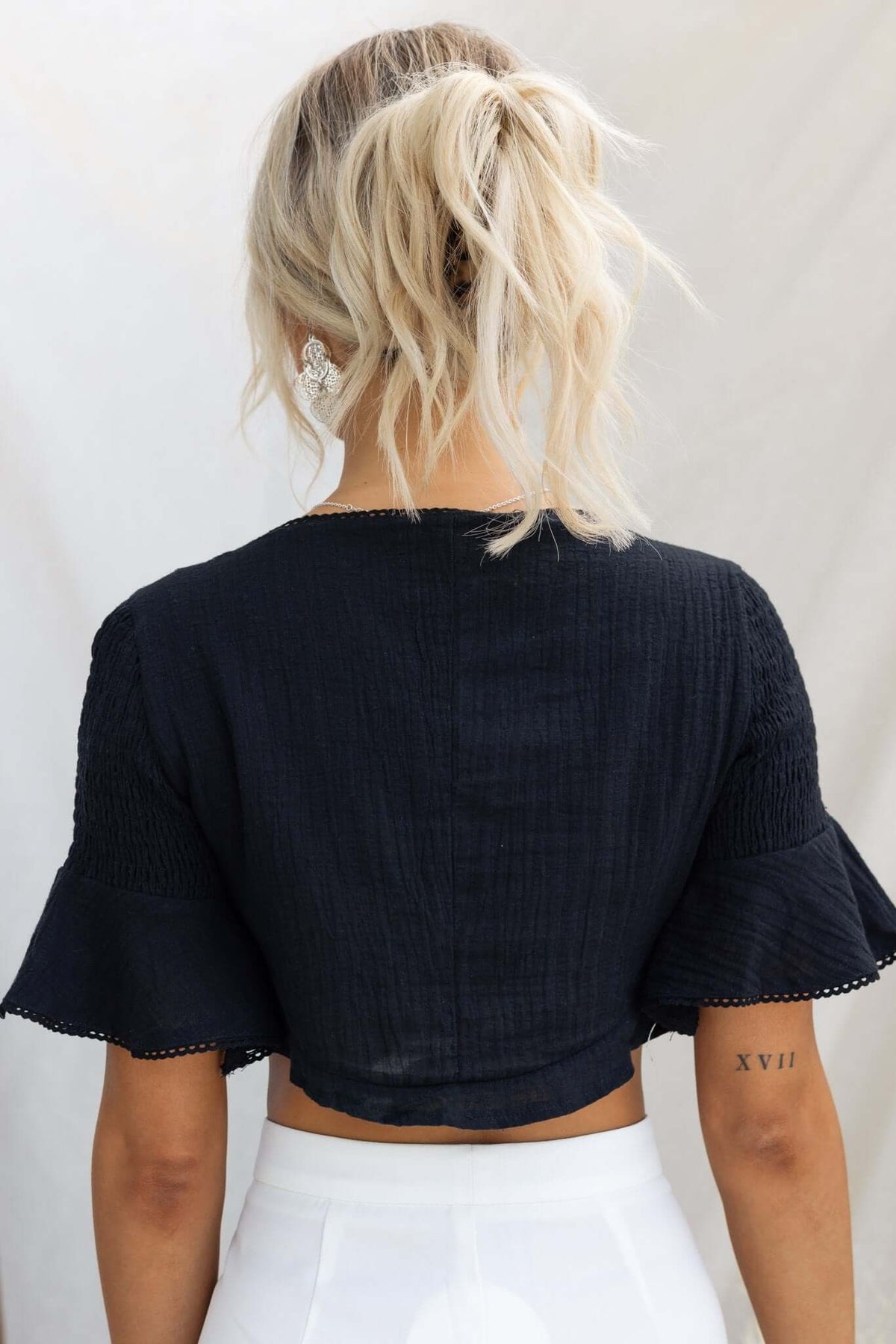 Back view of a black Dore Top with tie at bust and elastic sleeves, styled with white bottoms.
