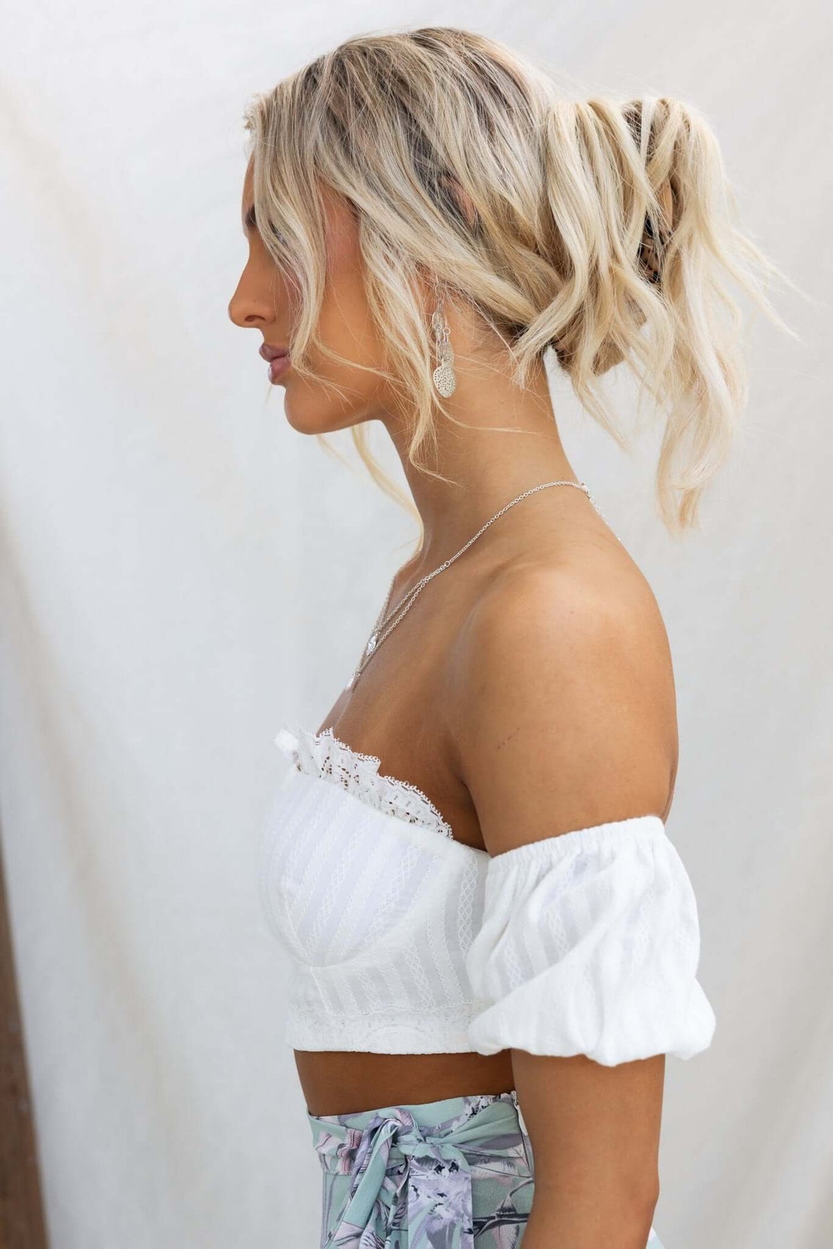 Profile view of a woman wearing the Giulia Top, a white off-shoulder top with puffed sleeves and a padded bust.