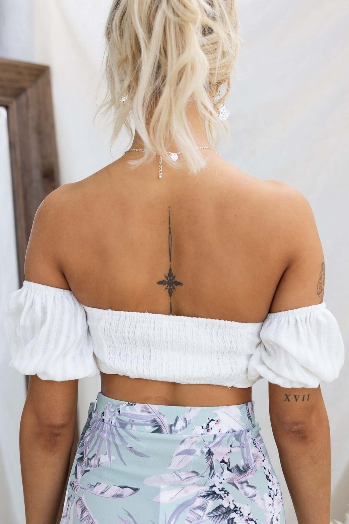 Woman wearing Giulia Top, showing back with off-shoulder elastic cuffs and patterned skirt.