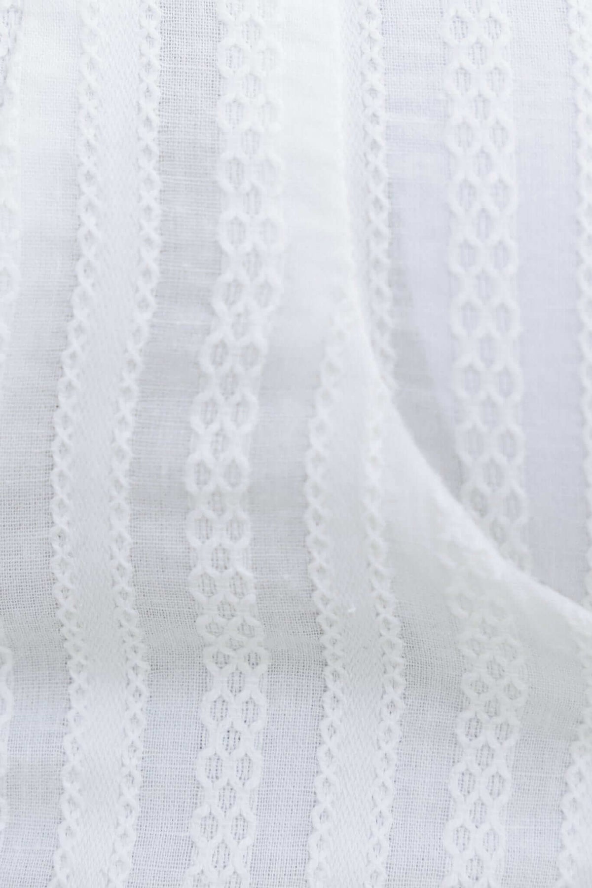 Close-up of textured white fabric with delicate vertical stripes and intricate lace detailing.