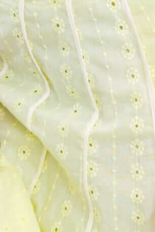 Close-up of soft yellow Anglaise fabric with floral patterns and delicate white edging.