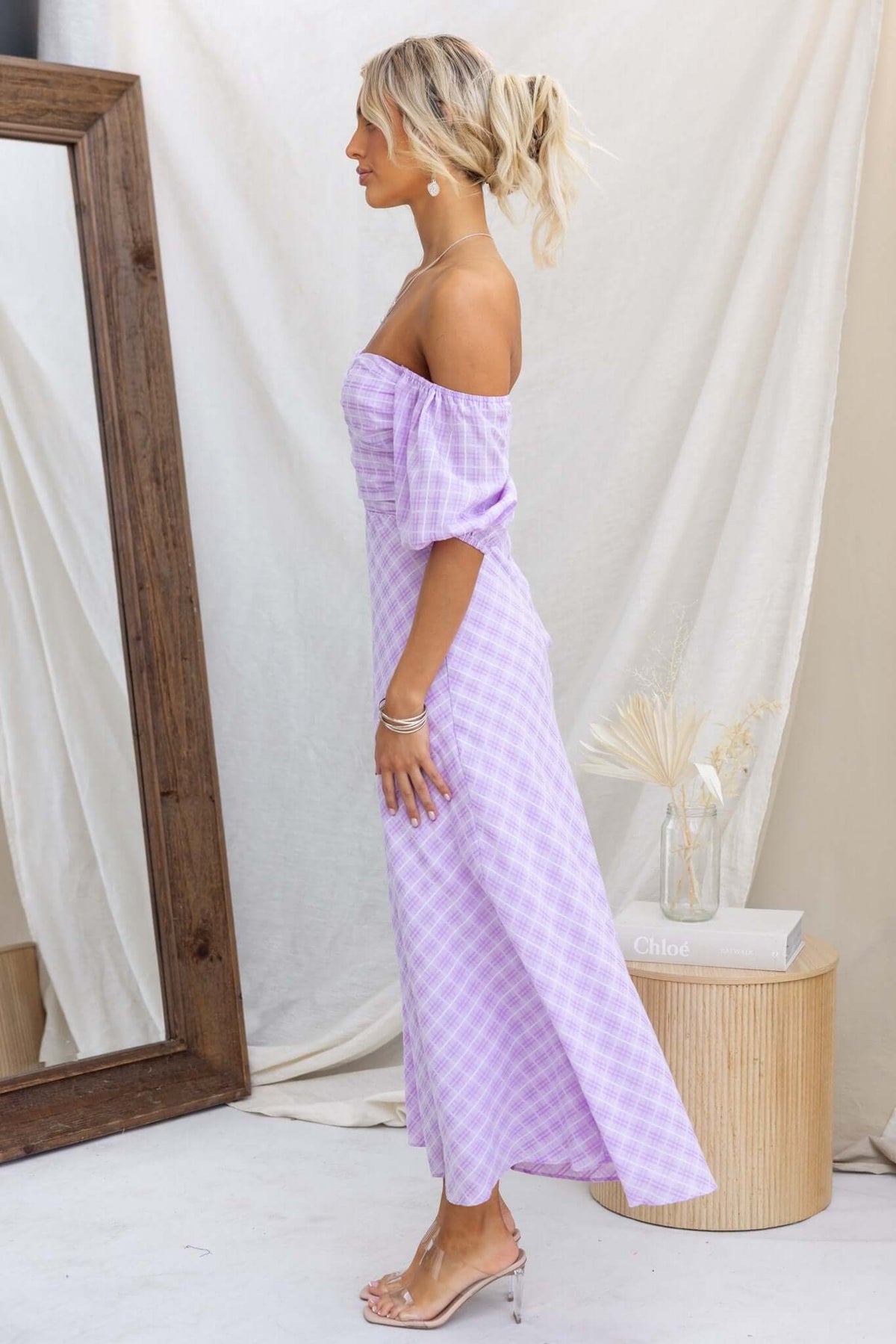 Model in Elayna Maxi Dress, a lavender gingham off-shoulder dress with cutouts and elastic sleeves, styled elegantly.