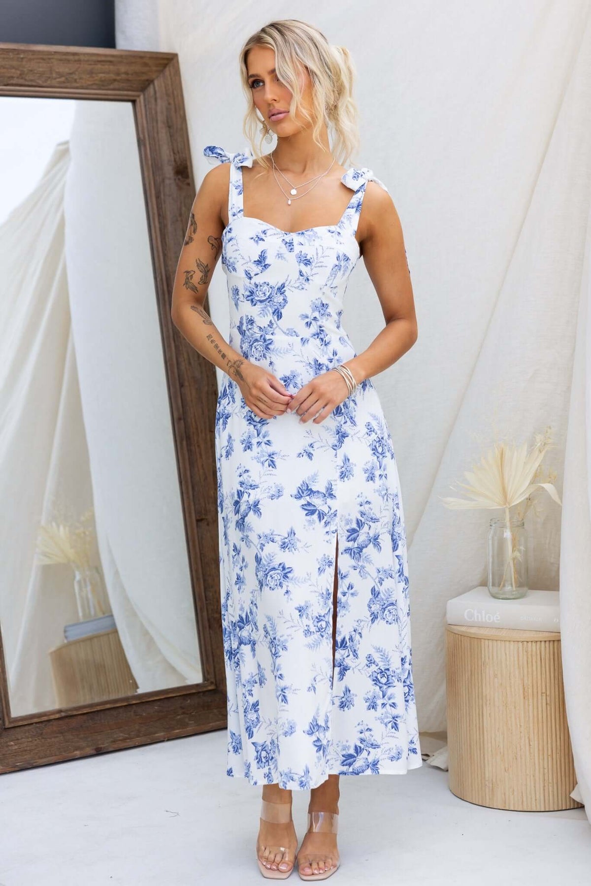 Model wearing Prescott Midi Dress with floral print, adjustable tie straps, and front split, in a stylish outdoor setting.