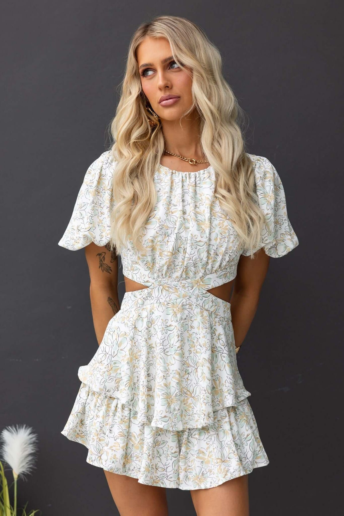 Model wearing a dewy floral playsuit with a cut-out back, puff sleeves, and tiered ruffles.