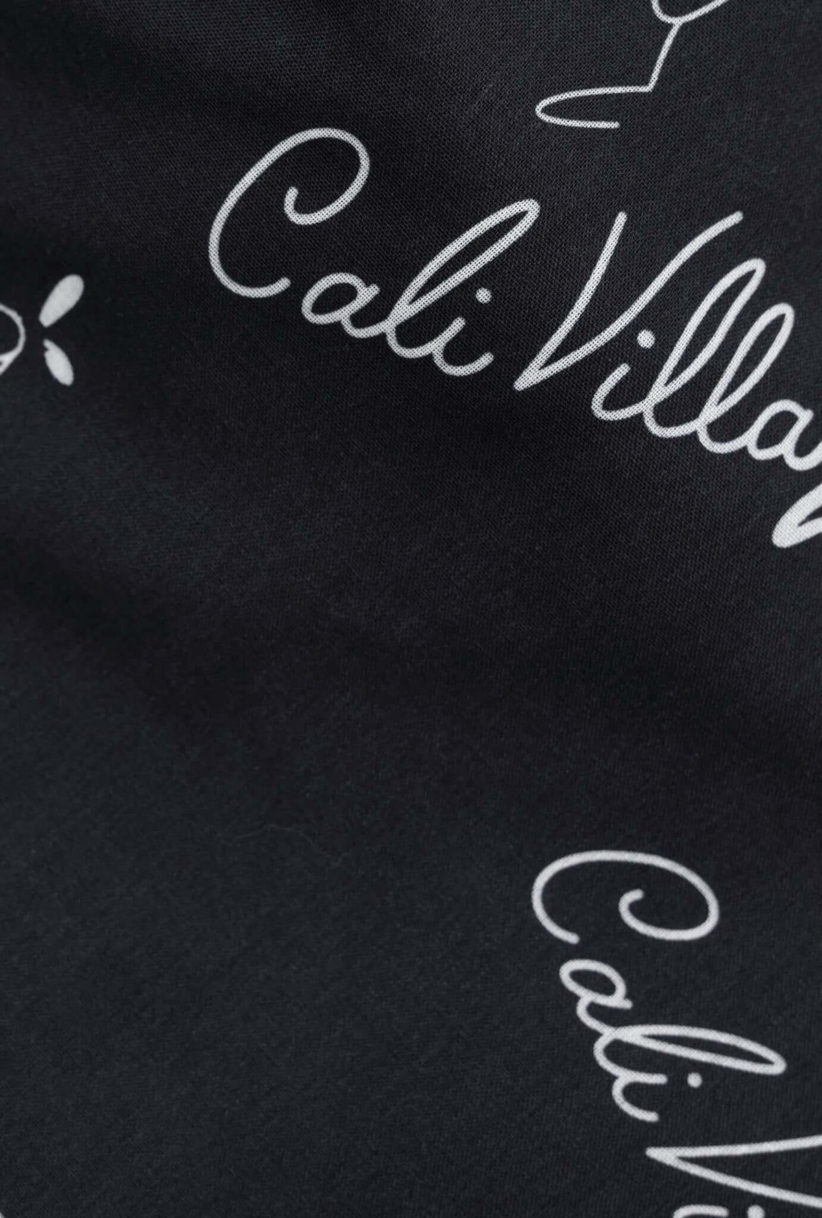 Close-up of fabric featuring white script text on a black background, highlighting Cali Village design.