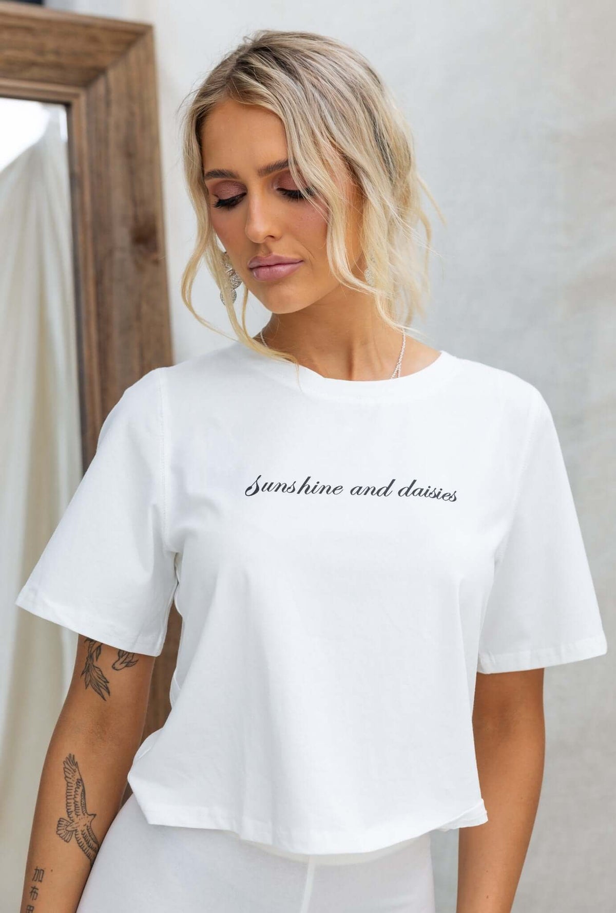 Model wearing a white Daisy Tee with 'sunshine and daisies' text, showcasing a relaxed boxy fit and round neckline.