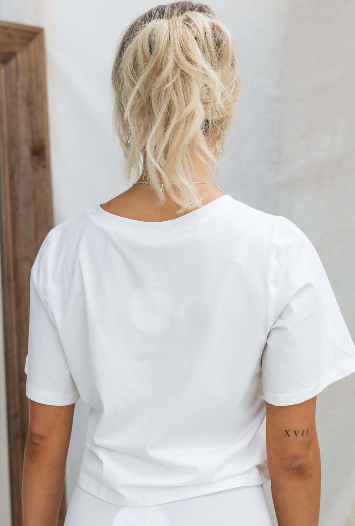 Back view of a woman wearing a white Daisy Tee with a round neckline and oversized fit.