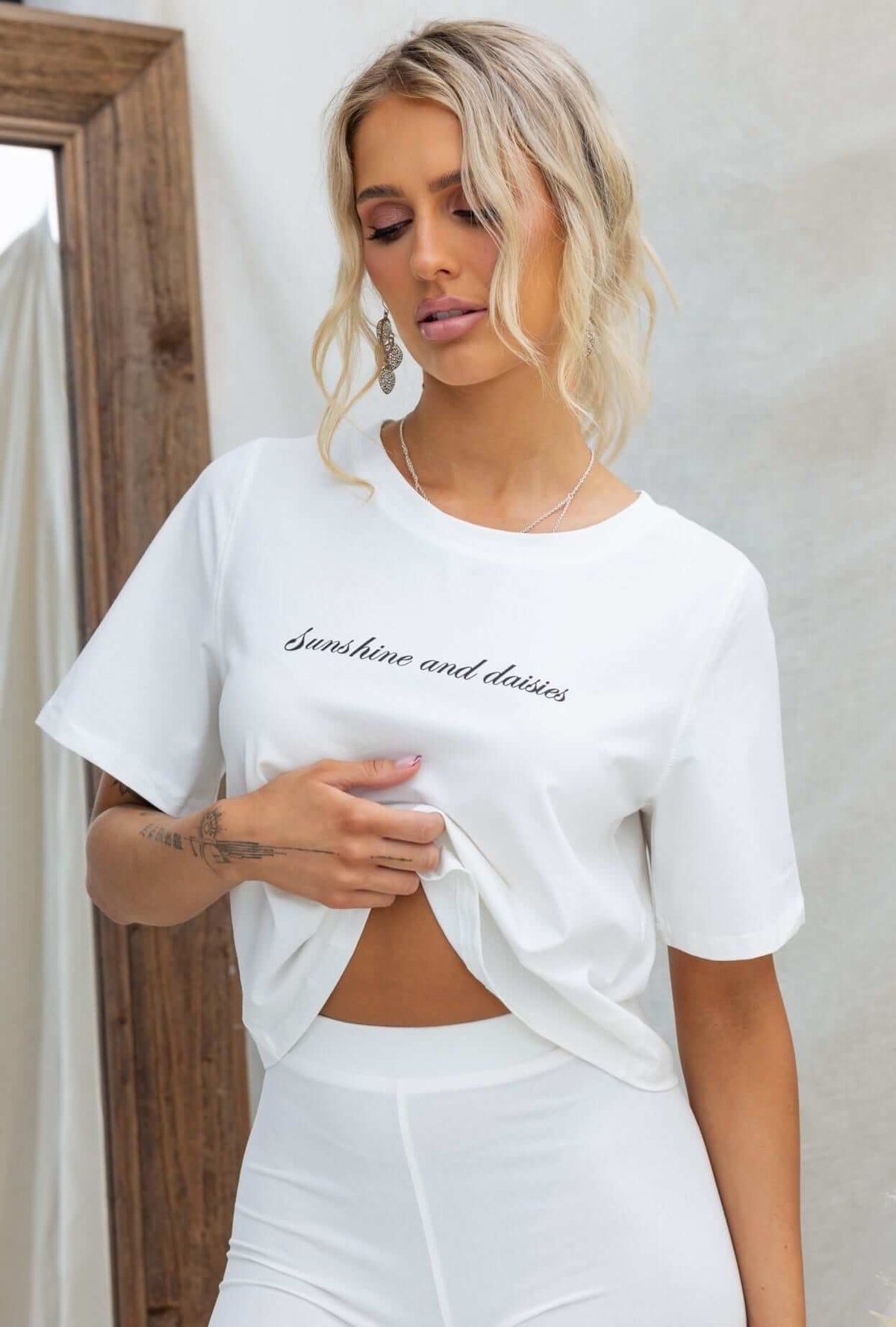 Model wearing a white Daisy Tee with round neckline and oversized fit, featuring 'Sunshine and daisies' print.