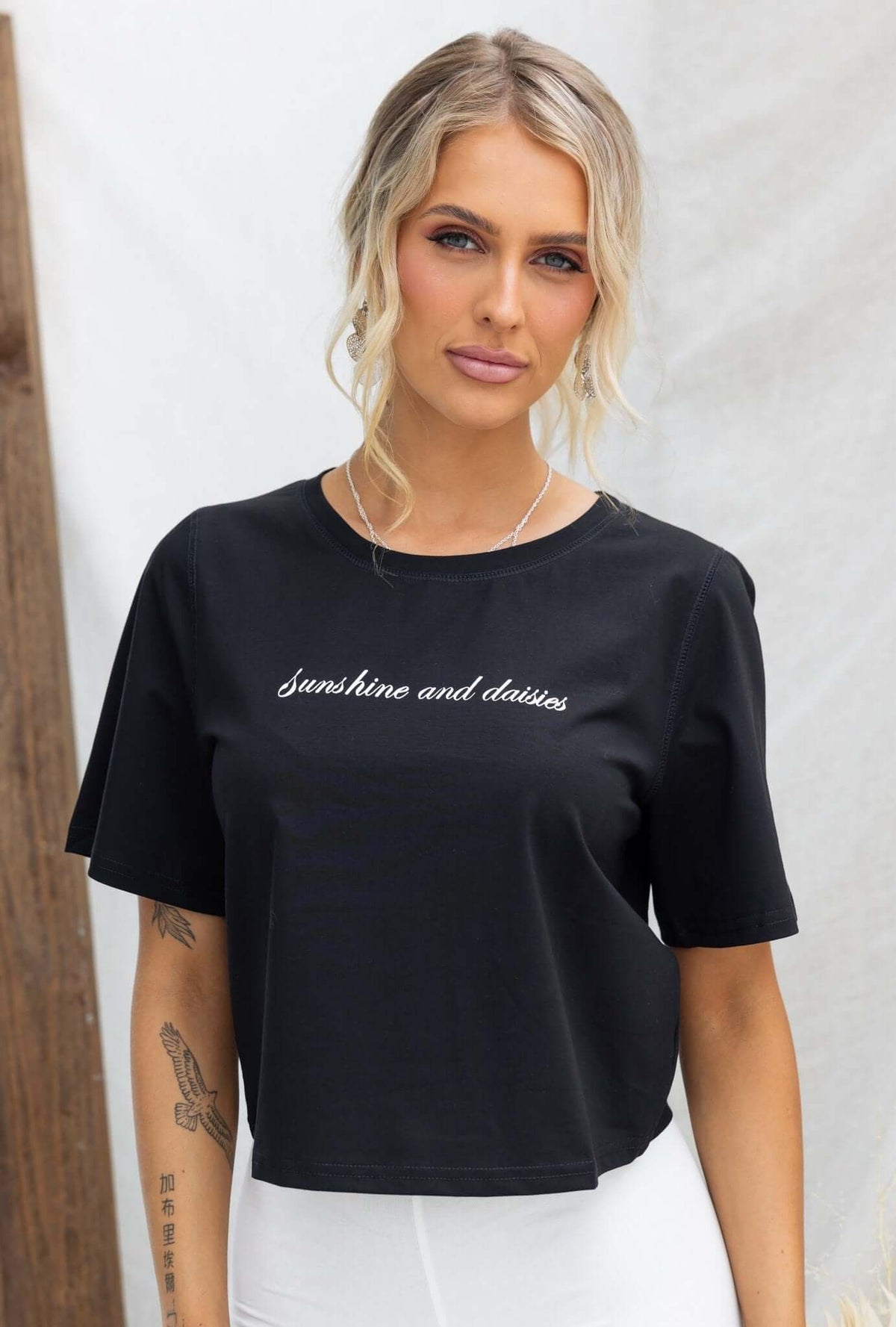 Model wearing a black Daisy Tee with 'Sunshine and daisies' text, showcasing a round neckline and relaxed fit.