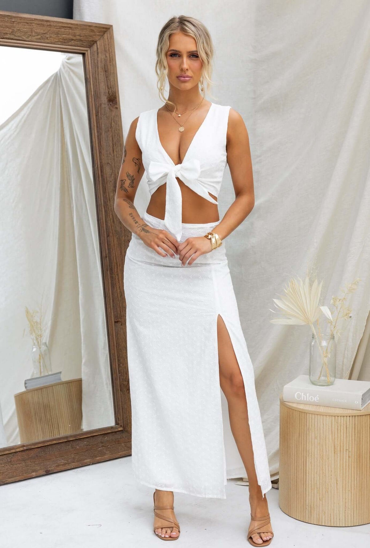 Model wearing an Olivine Top in white with tie bust and Anglaise fabric, paired with a fitted skirt in a stylish setting.