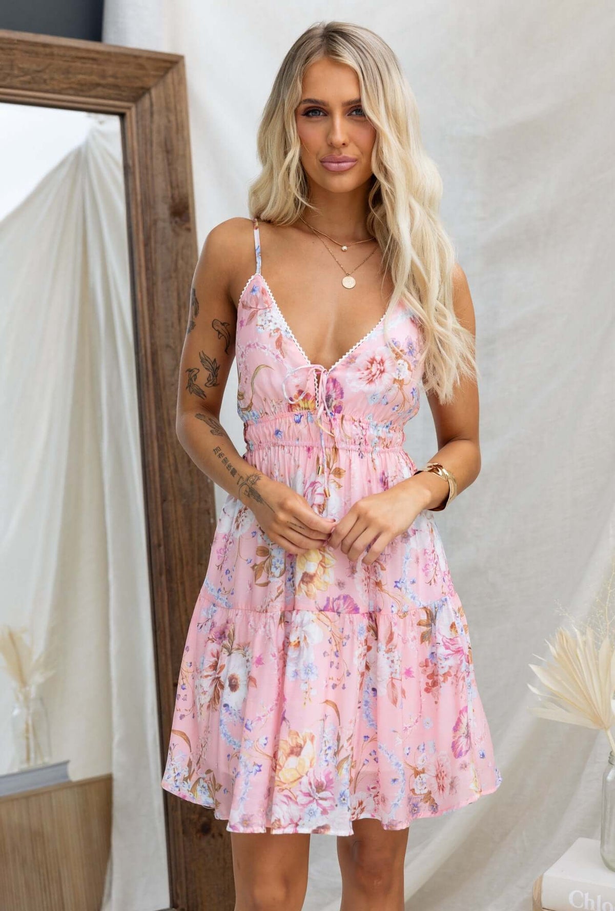 Garlyn dress with adjustable straps and tie bust, featuring a floral pink design, modeled by a woman in a stylish setting.