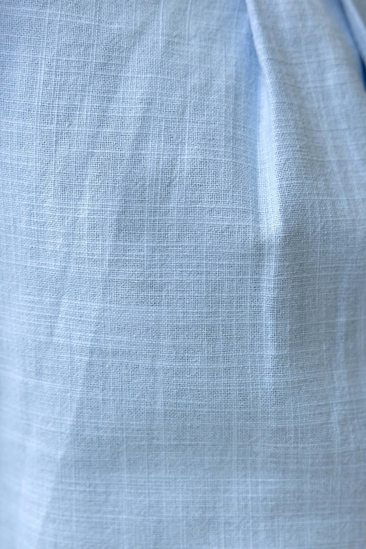 Close-up of lightweight blue fabric with a textured weave, showcasing its softness and cotton-like feel.