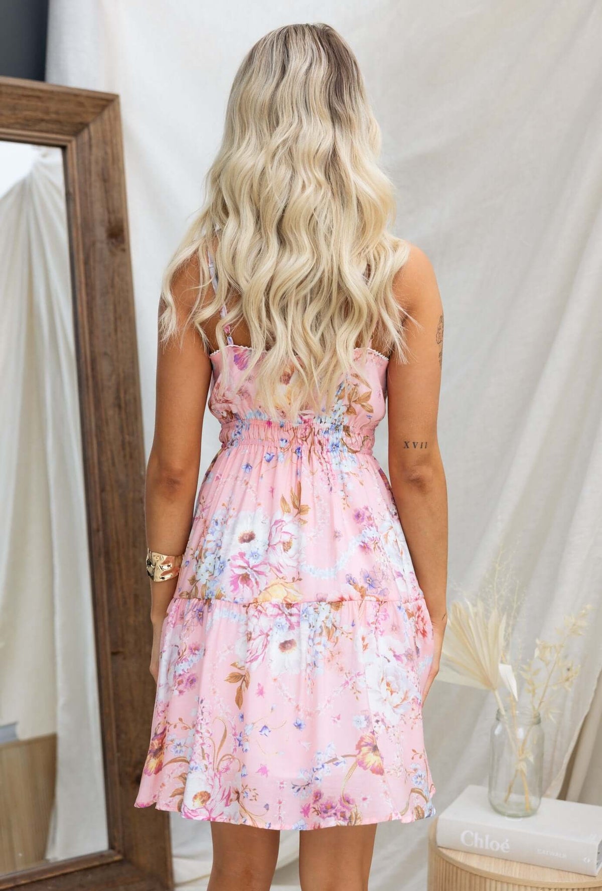 Back view of a woman in a pink floral Garlyn dress with adjustable straps and an elastic waistband.