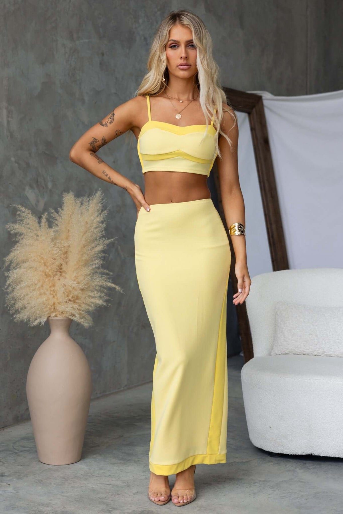 Model wearing the Rianna Top in yellow with adjustable straps and a fitted design, paired with a matching skirt.