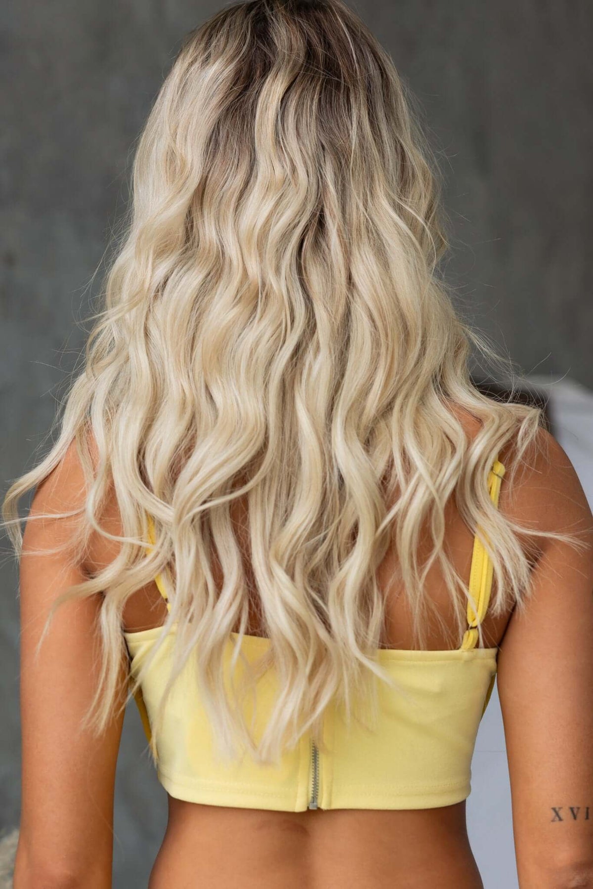 Back view of a woman wearing a yellow Rianna Top with adjustable straps and wavy blonde hair, showcasing the stylish design.