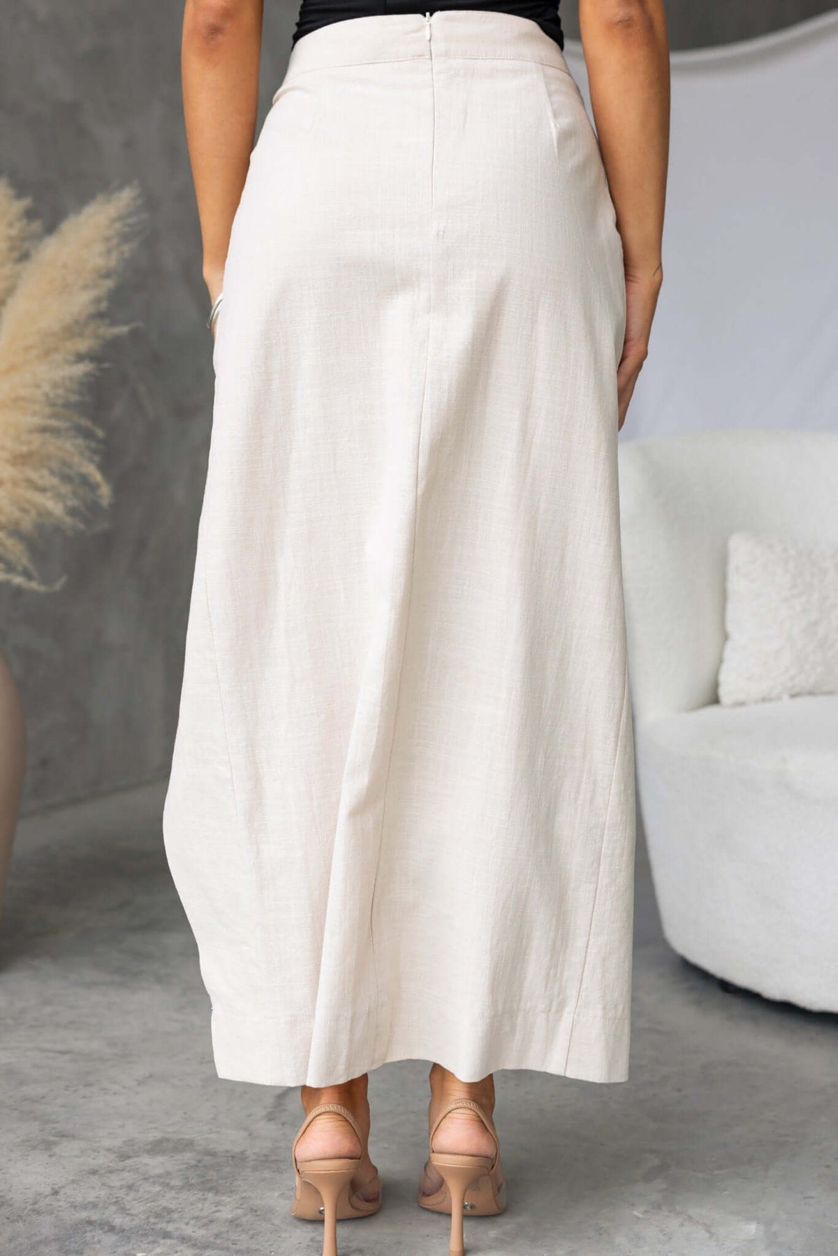 Back view of Ferris Maxi Skirt in cream, featuring a mid-high waist and faux buttons, styled with heels.