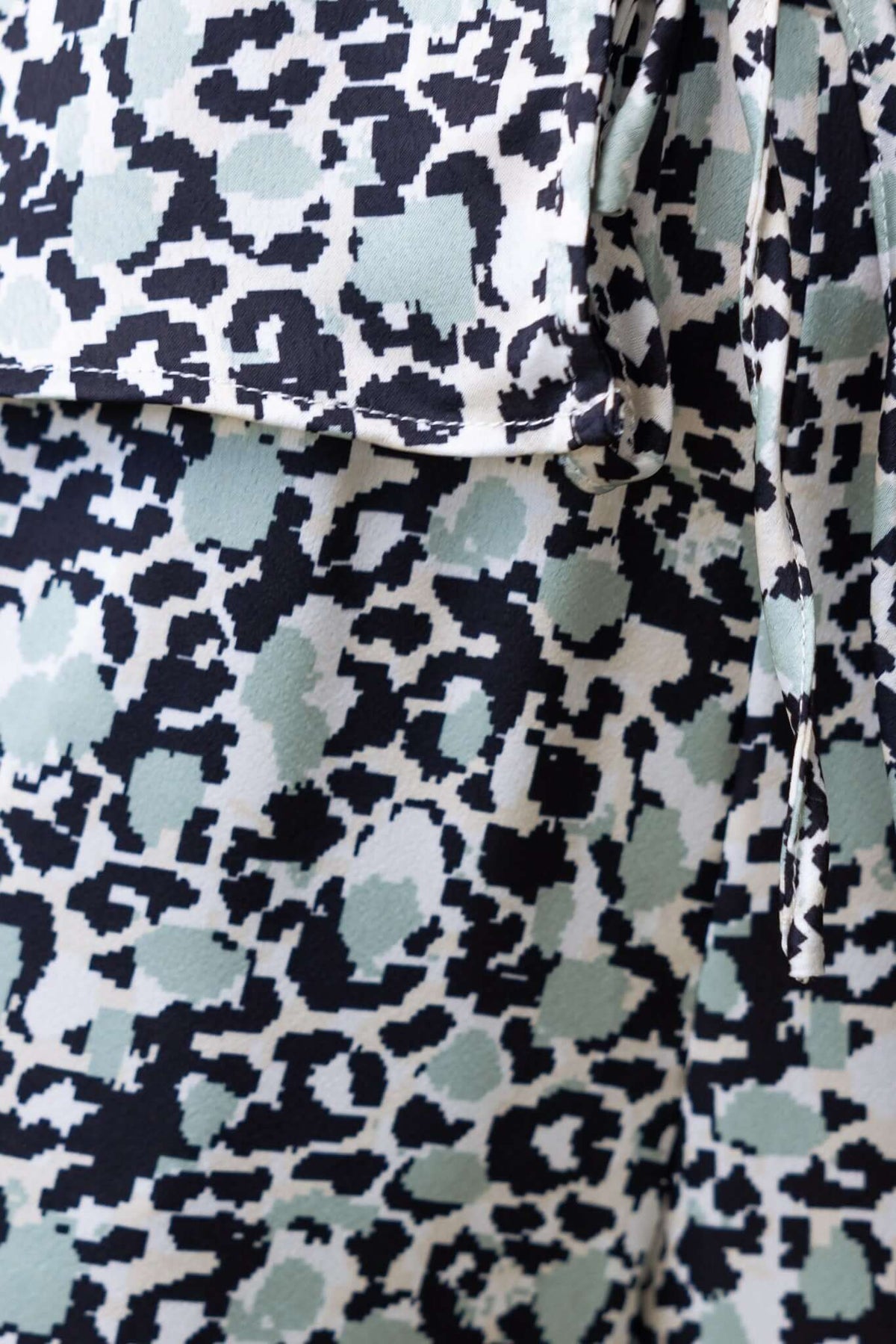 Close-up of Nyah Top in a black and mint animal print pattern with a tie detail at the bust.