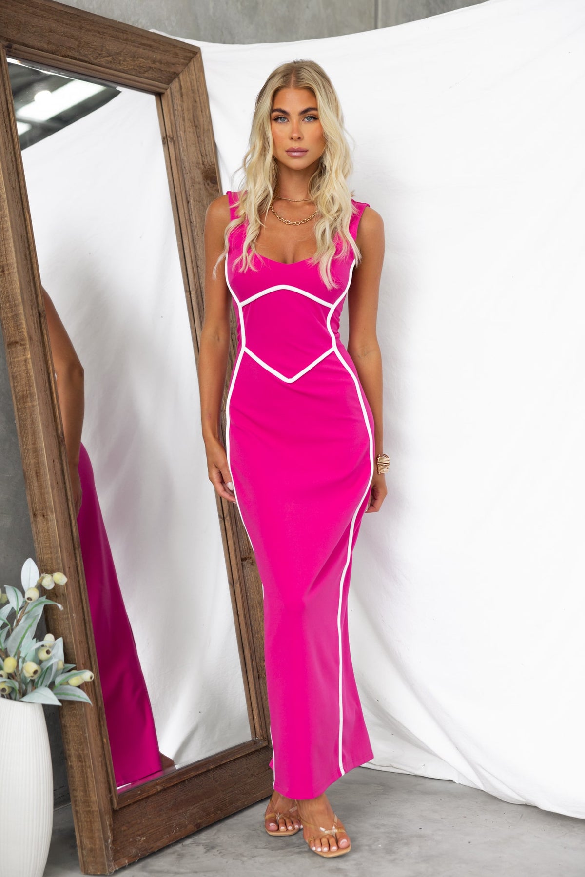 Model wearing a fuchsia bodycon maxi dress with white accents and a back split, showcased in front of a mirror.