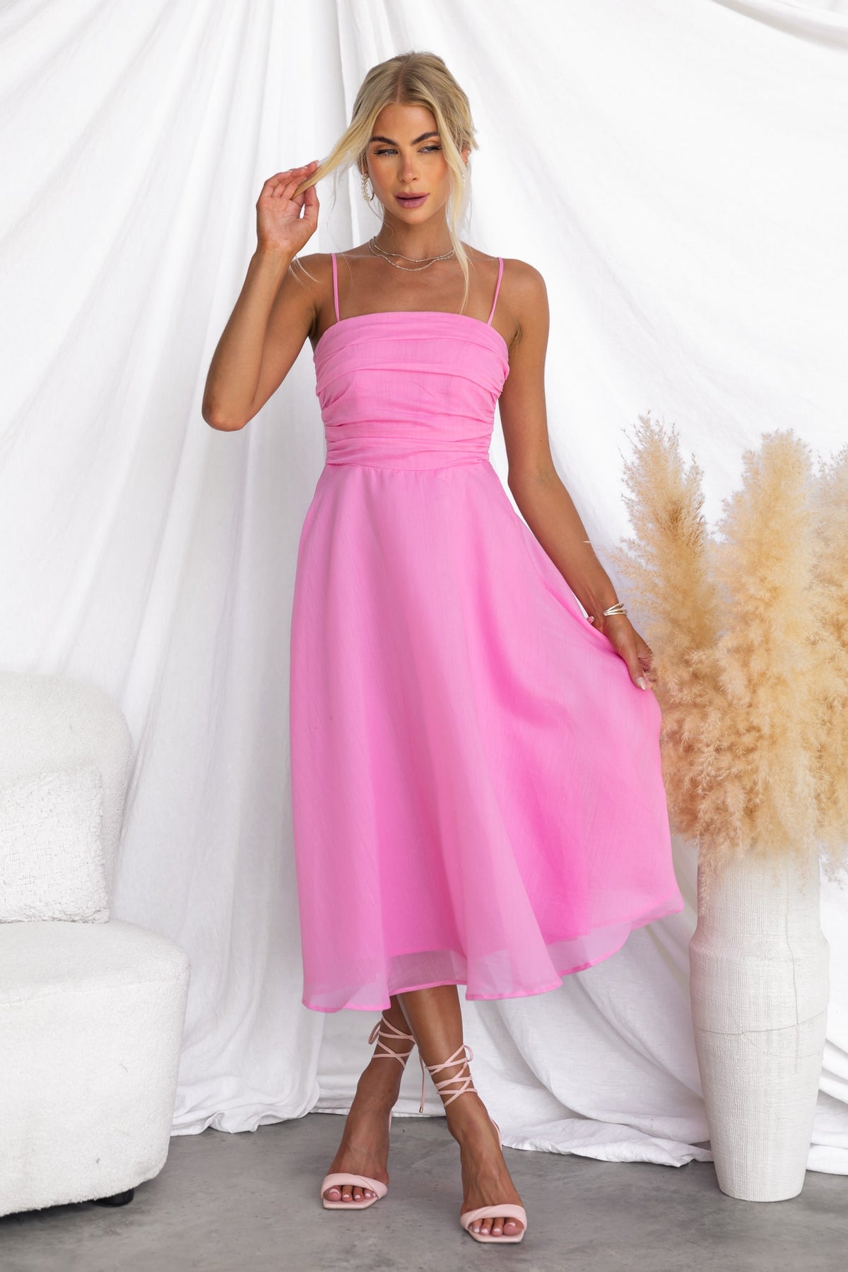 Model wearing Reilan Midi Dress in pink chiffon with adjustable straps and a flowy design, posing against a soft backdrop.