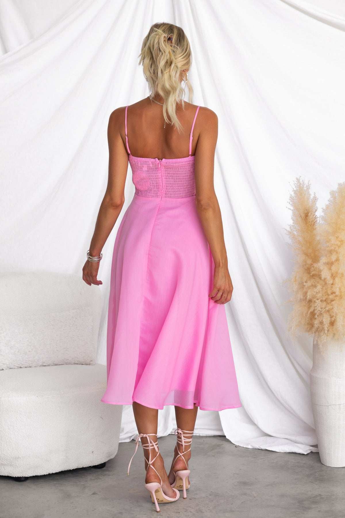 Back view of Reilan Midi Dress in pink with adjustable straps and smocked detailing, styled with elegant heels.