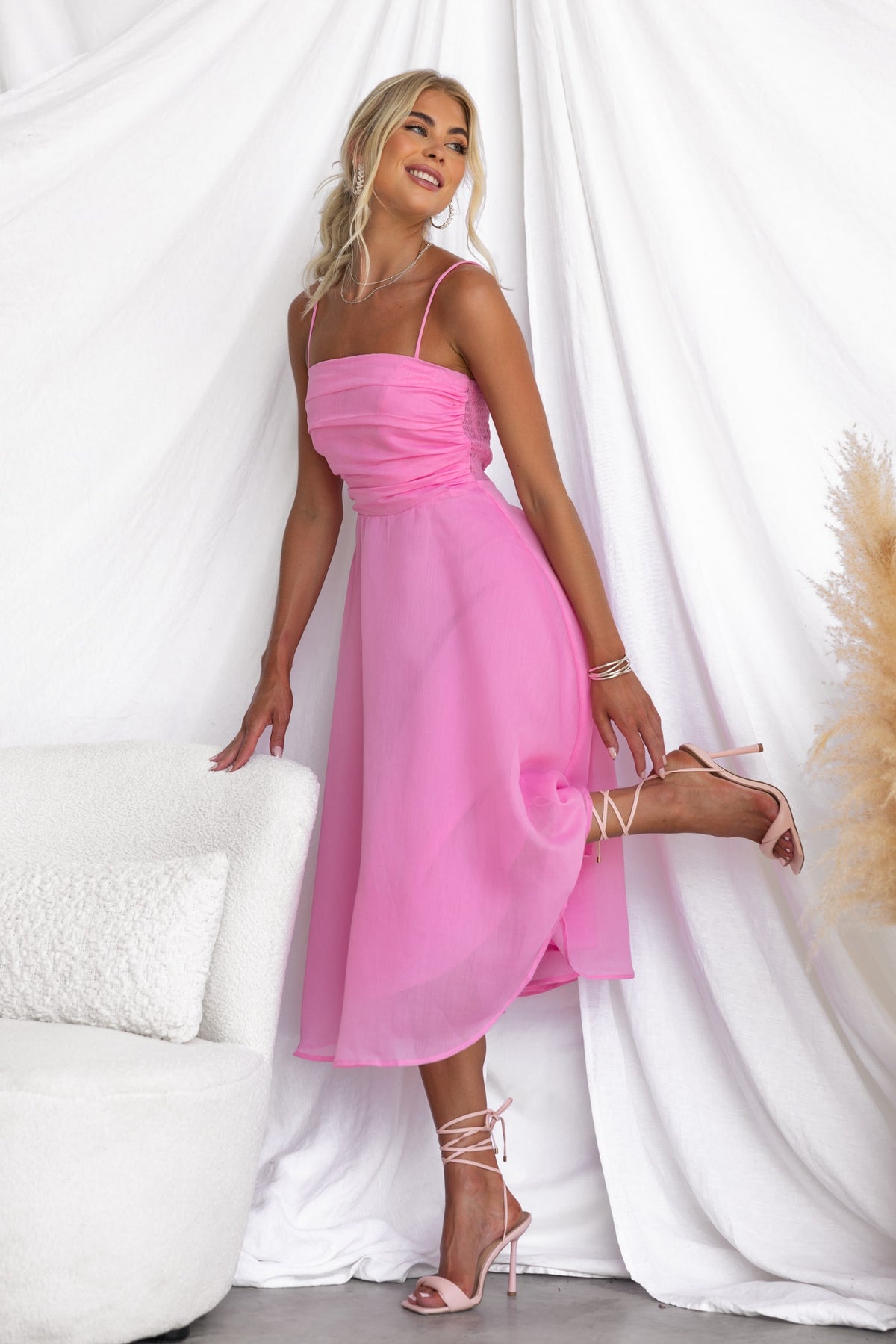 Model wearing a pink Reilan midi dress with adjustable straps and chiffon material, posing elegantly against a white backdrop.
