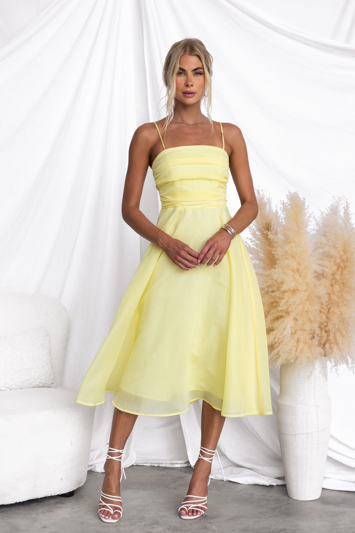 Elegant Reilan Midi Dress in yellow, featuring adjustable straps and chiffon fabric, styled with strappy heels.