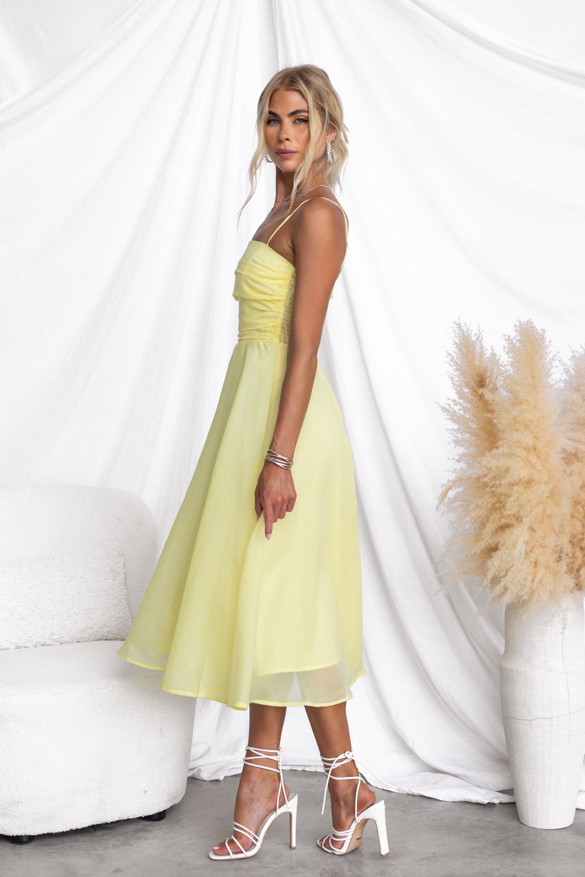 Model wearing a Reilan Midi Dress in soft yellow, featuring adjustable straps and a flowing chiffon skirt.