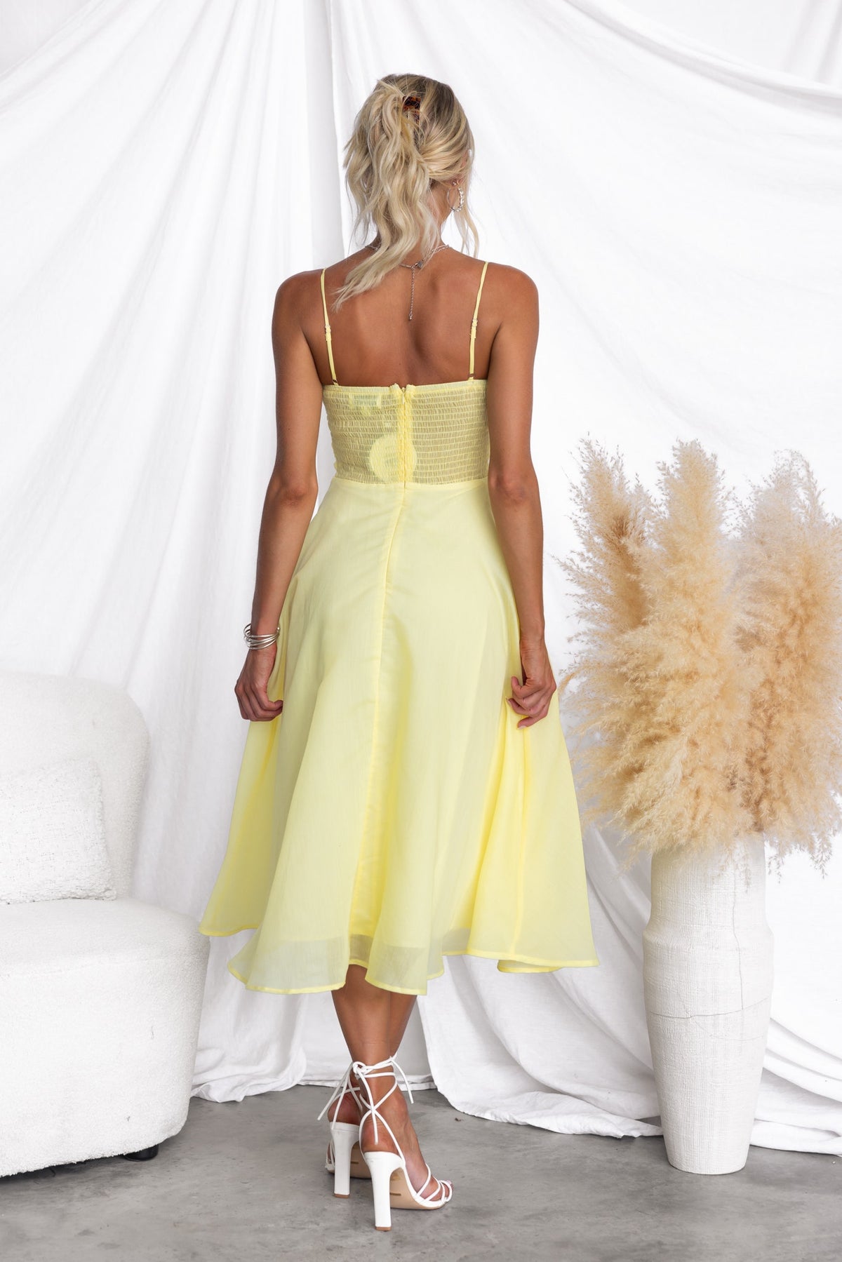 Back view of a woman in a yellow Reilan Midi Dress with adjustable straps and chiffon fabric.