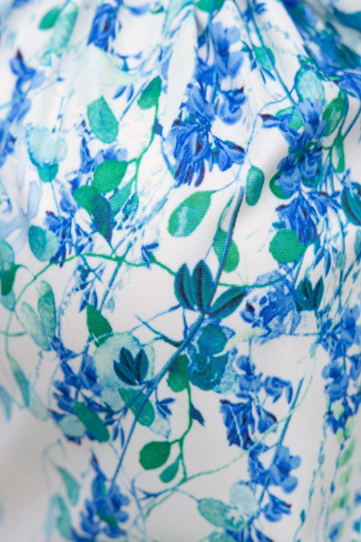 Close-up of Bruna Shirt's floral print featuring blue flowers and green leaves on a light background.
