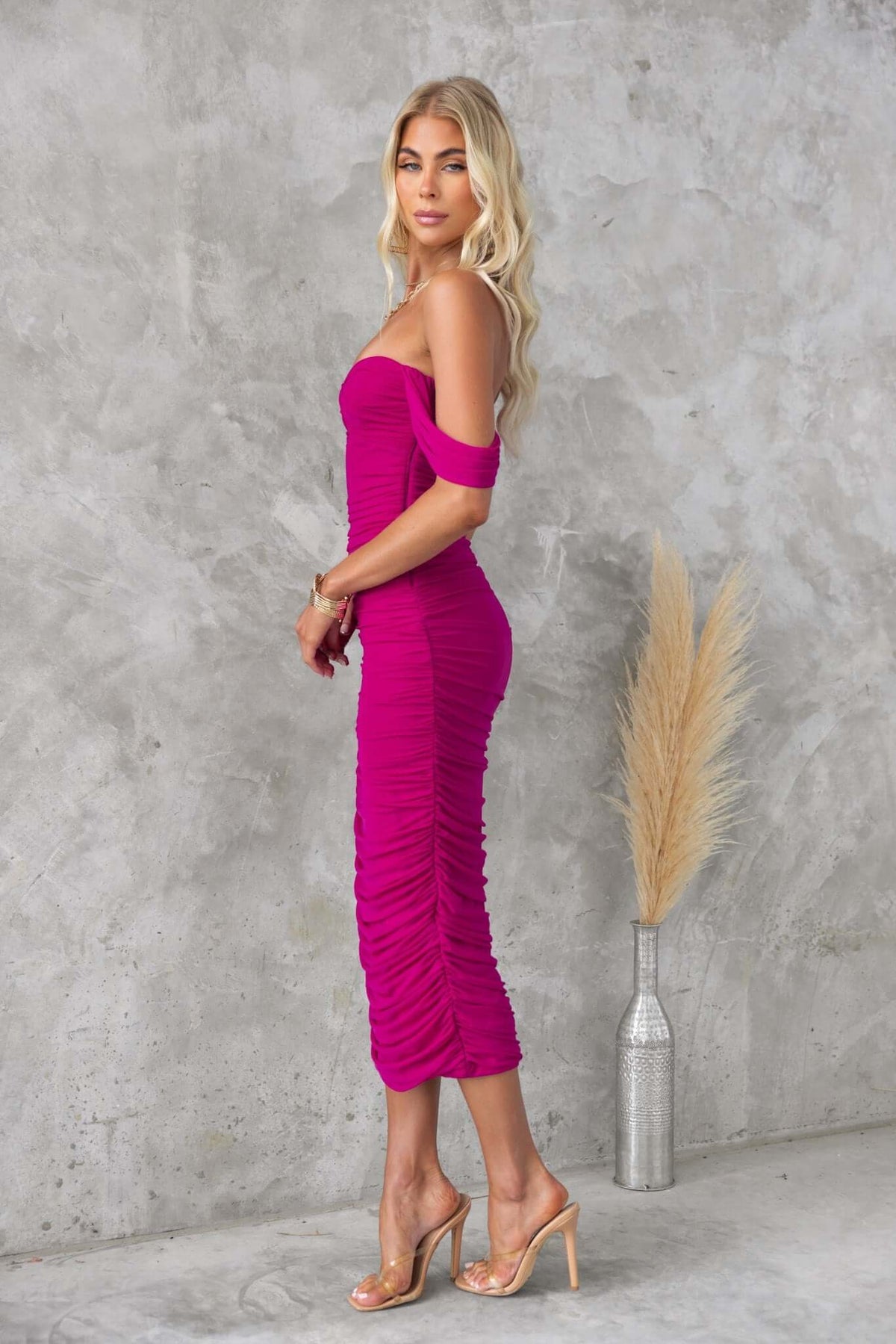 Vibrant pink bodycon Ledger Midi Dress with ruching and a mesh overlay, styled with transparent heels.