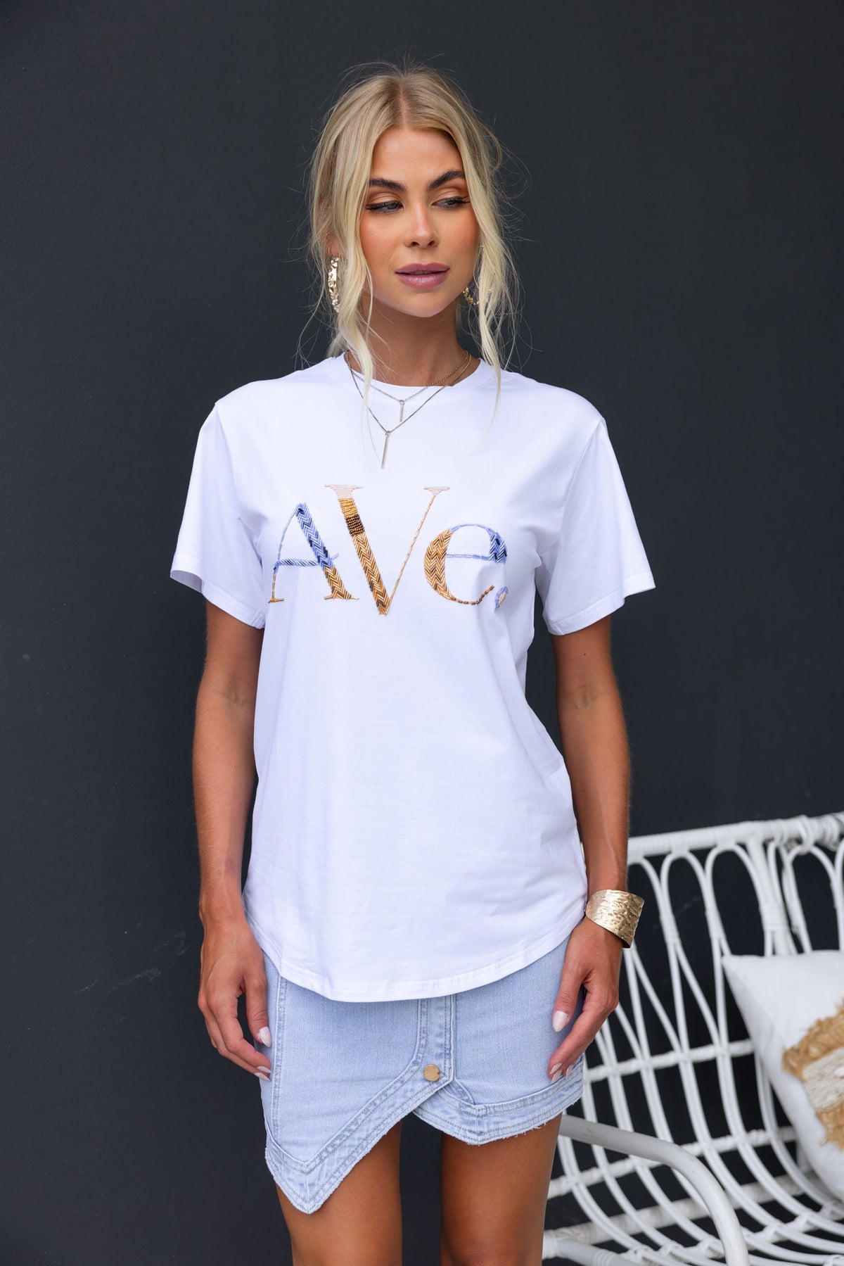 Model wearing white Ave print tee with round neckline, paired with denim skirt, showcasing casual style.