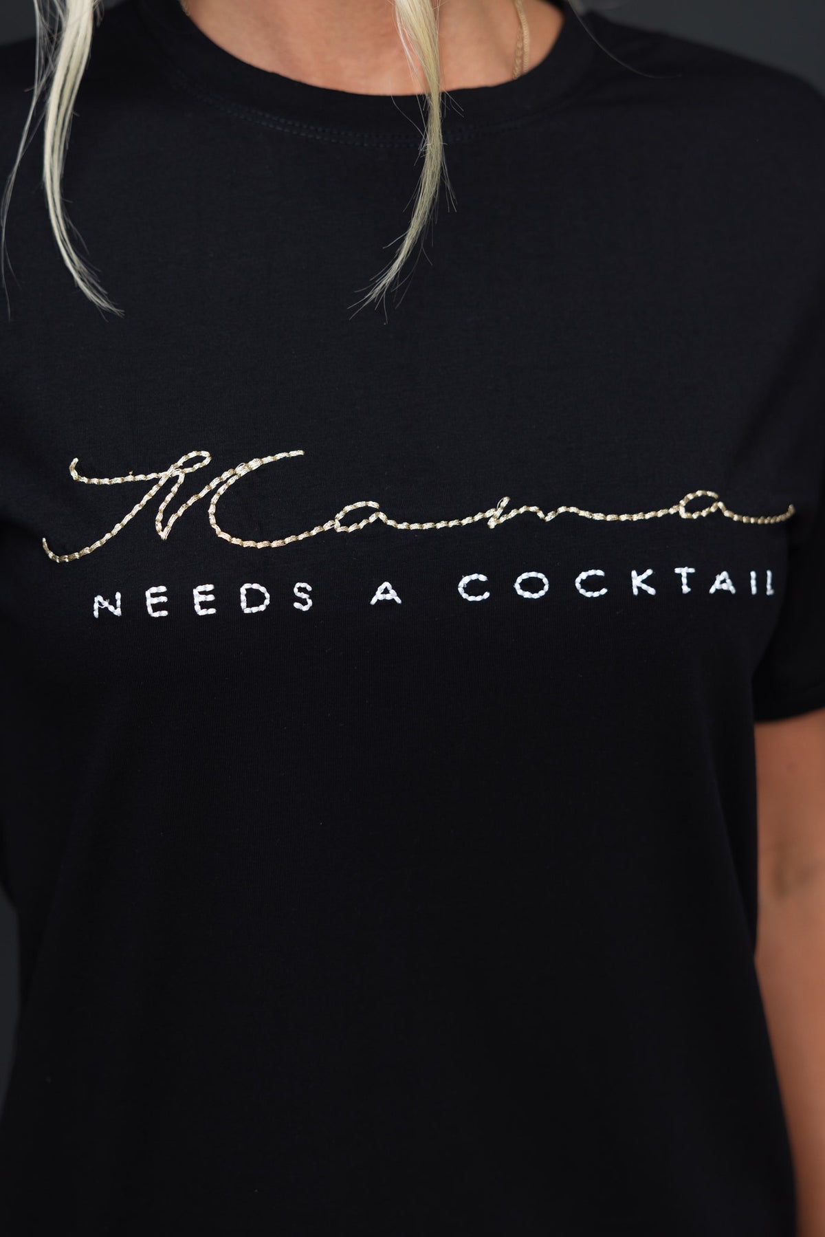 Black Kapri Tee featuring 'Mama needs a cocktail' in metallic threading, soft cotton, and standard fit.