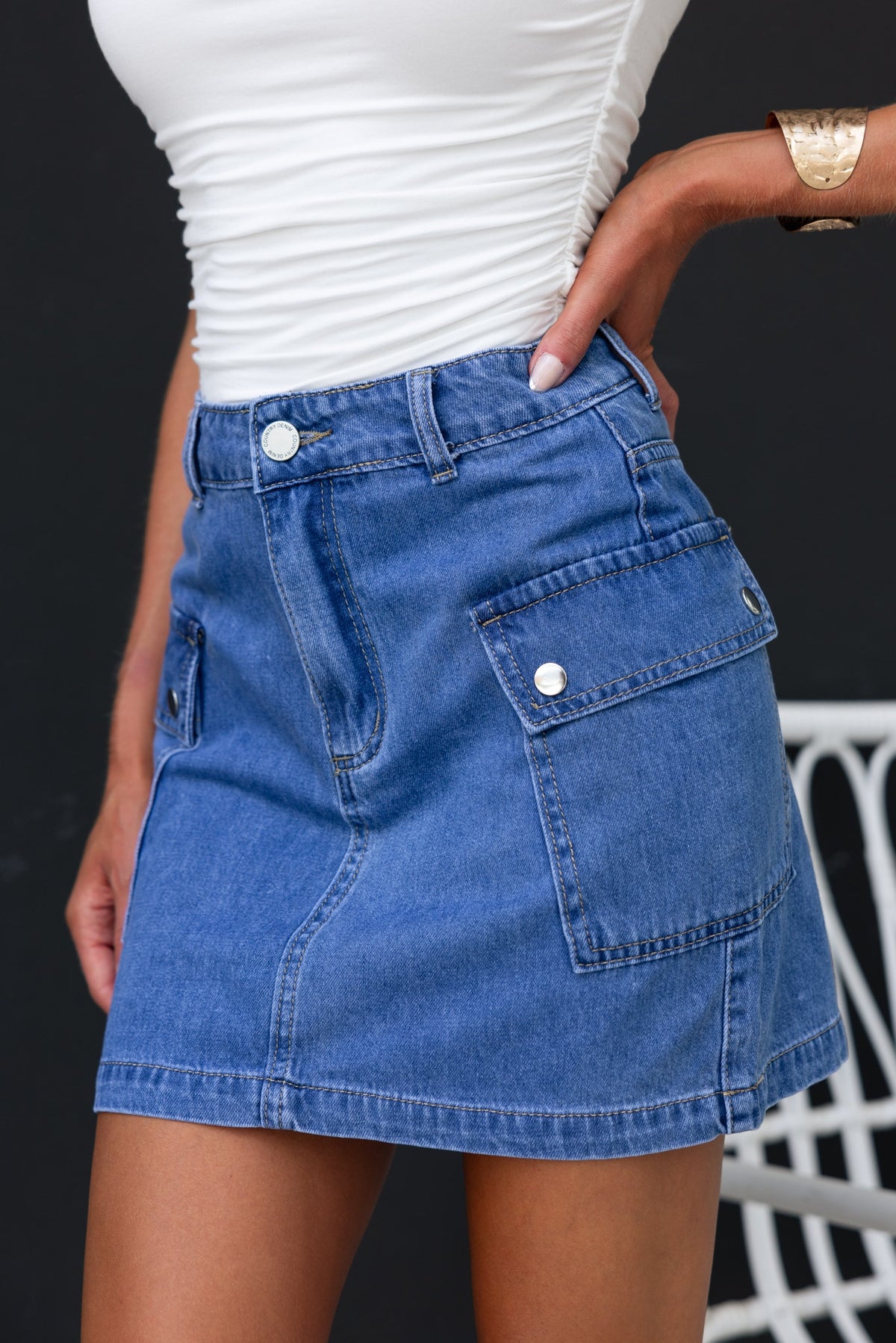 Rubi denim skirt featuring cargo style pockets, standard fit, and made of 100% cotton, worn with a stylish top.