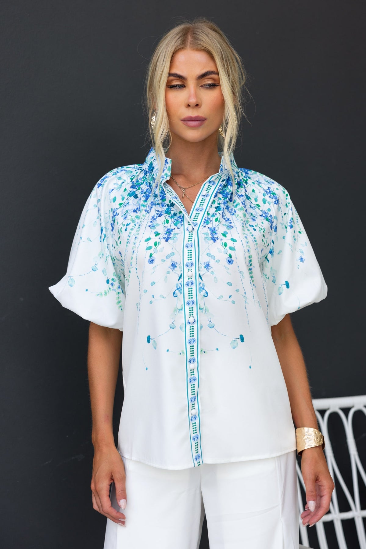 Bruna Shirt featuring a floral print, high neckline, and button-up front, worn by model styled with light pants.
