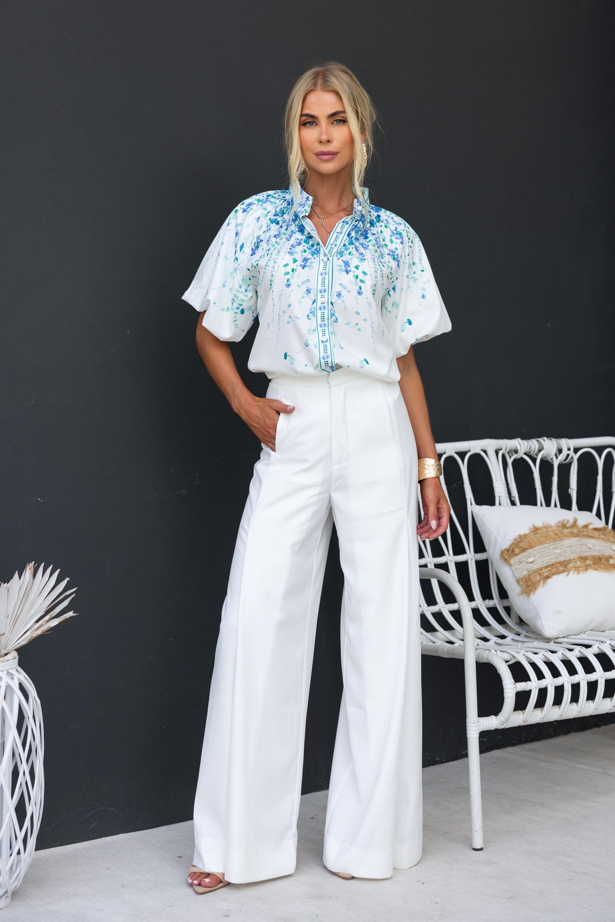 Model wearing Bruna Shirt with floral print and puffed sleeves, paired with white wide-leg pants in stylish indoor setting.