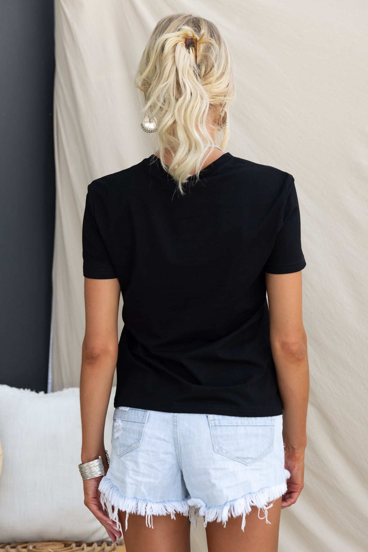 Model wearing the Wyatt Tee in black, featuring a round neckline and soft cotton feel, paired with denim shorts.