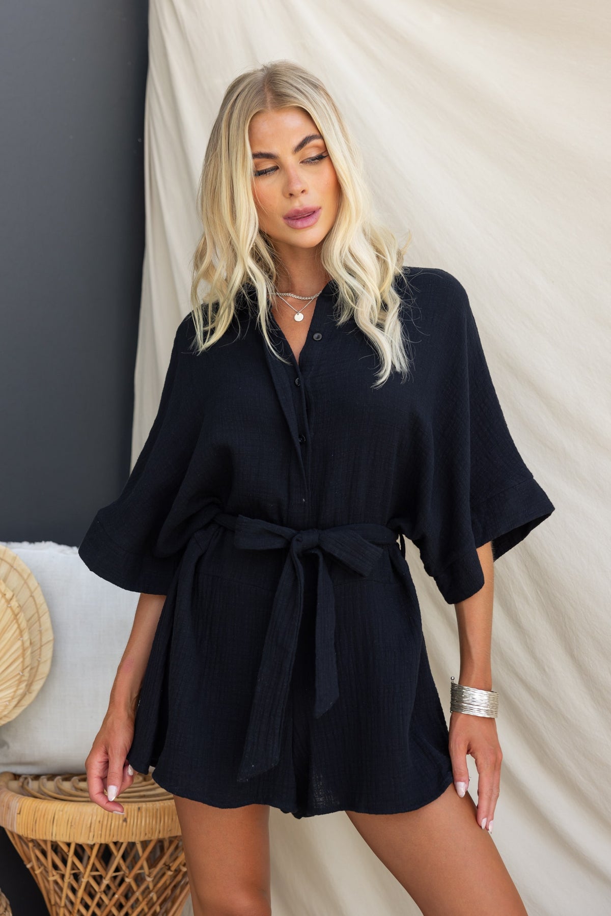 Model wearing a black Rowson playsuit with a collar, button-up front, and removable fabric tie, styled in a relaxed fit.