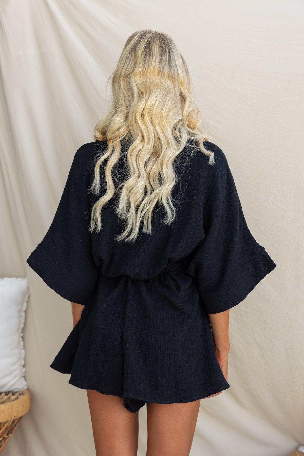 Back view of a black Rowson playsuit with a relaxed fit and removable tie, worn by a model with long wavy hair.