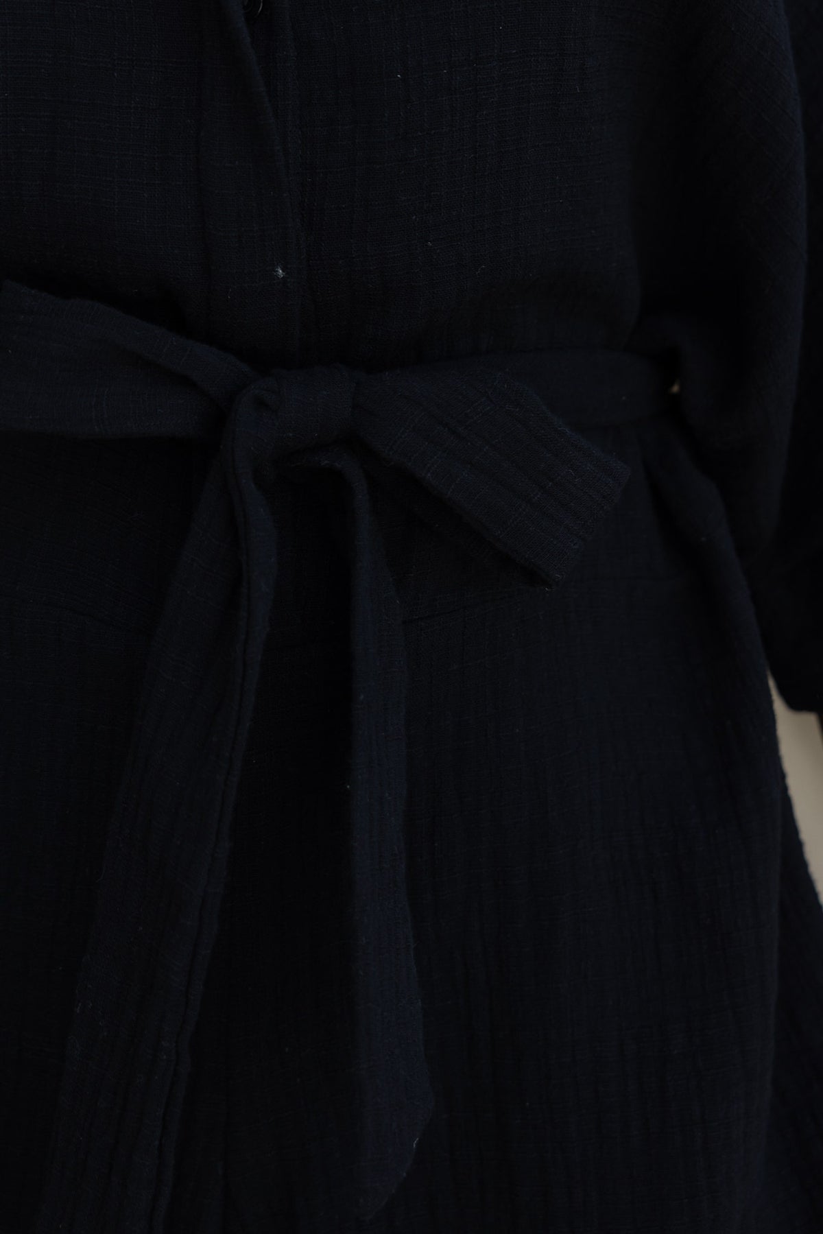 Close-up of the Rowson Playsuit in black, featuring a removable fabric tie around the waist and textured material.