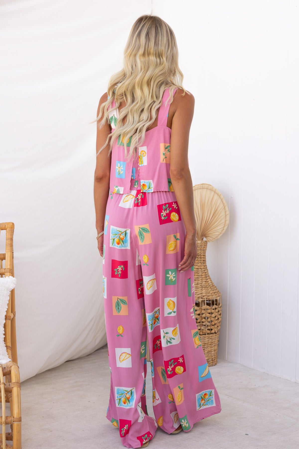 Back view of a model wearing a colorful abstract print Verko jumpsuit in pink, featuring an elastic waistband and pockets.