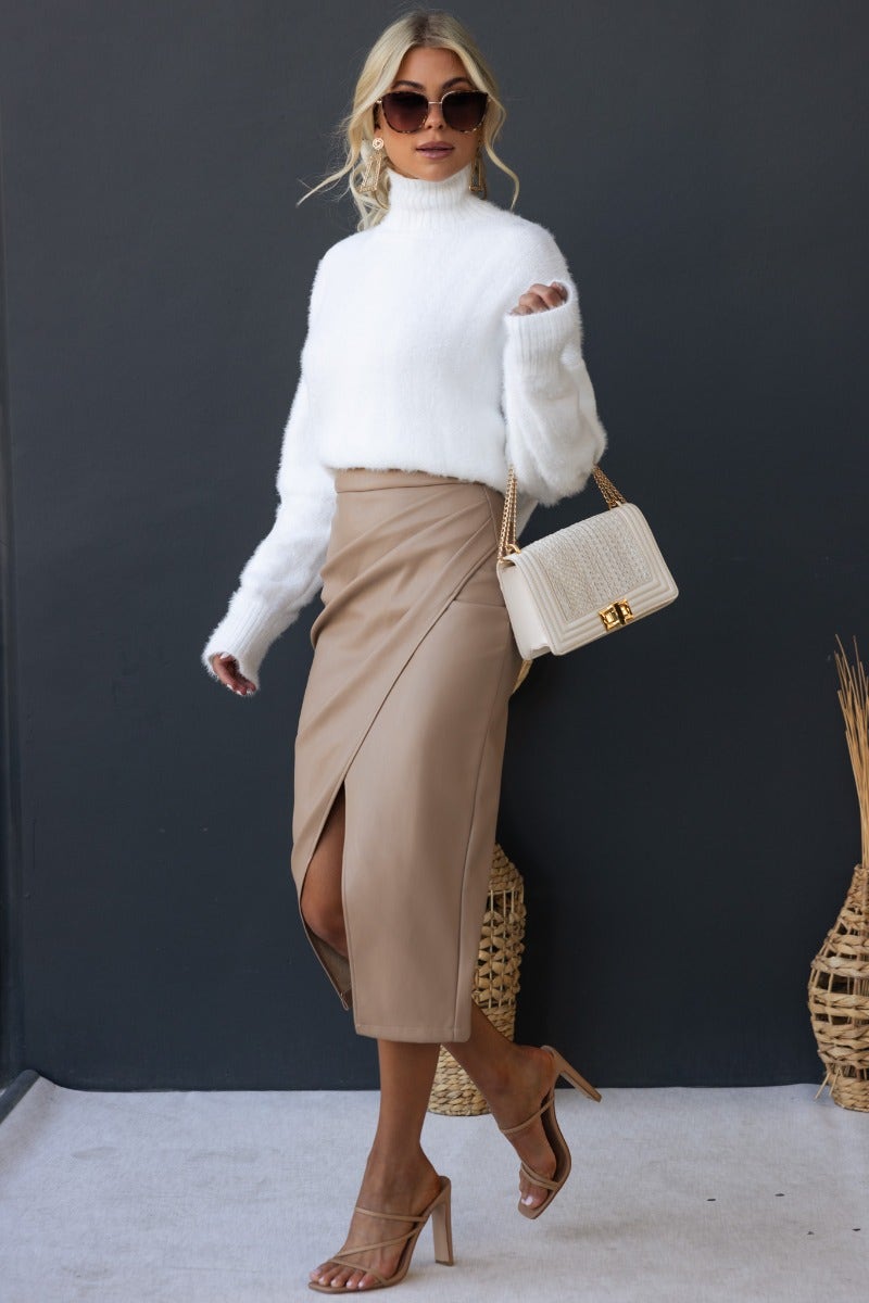 Model wearing the Qorinda Midi Skirt with a white sweater and handbag, showcasing faux leather and sleek design.