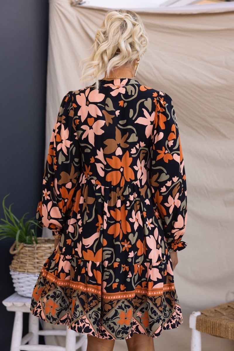Back view of the Stellan Dress, featuring a black base with colorful floral print, elastic cuffs, and a relaxed fit.