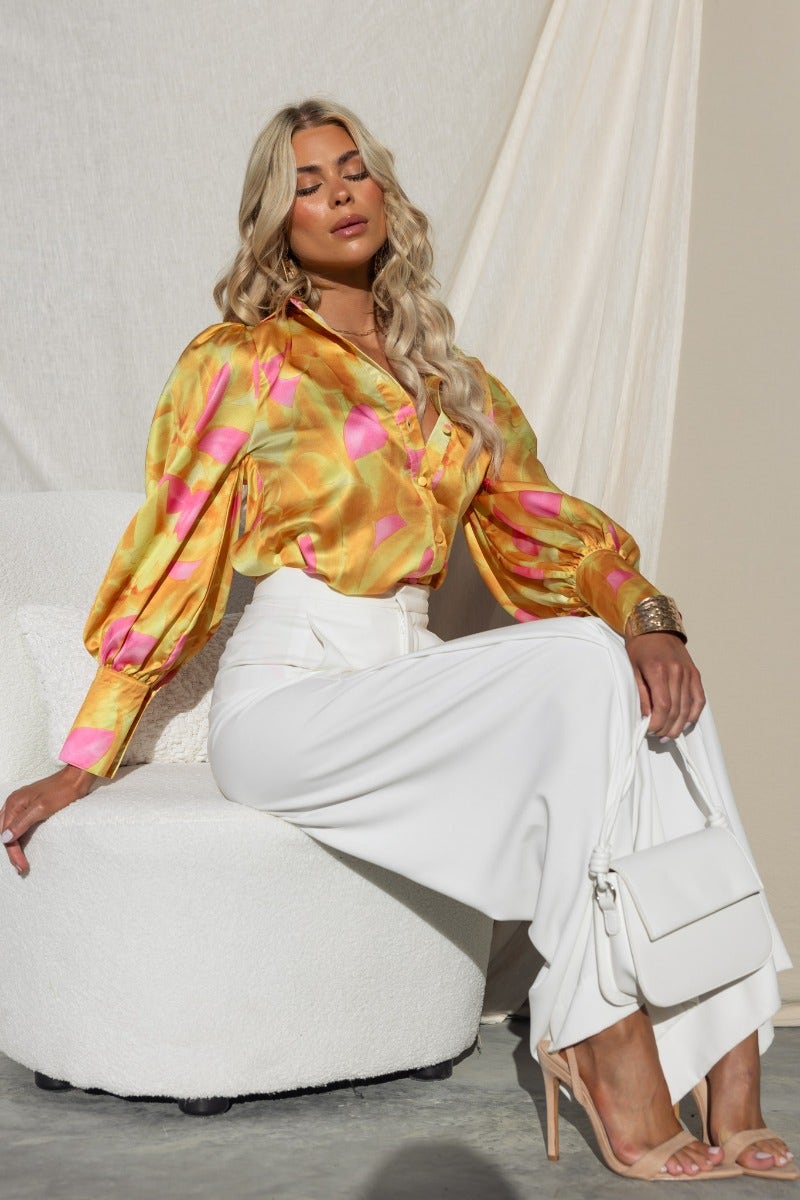 Model wearing Indianna Top, a vibrant satin button-up shirt, paired with a white skirt, showcasing a chic relaxed style.