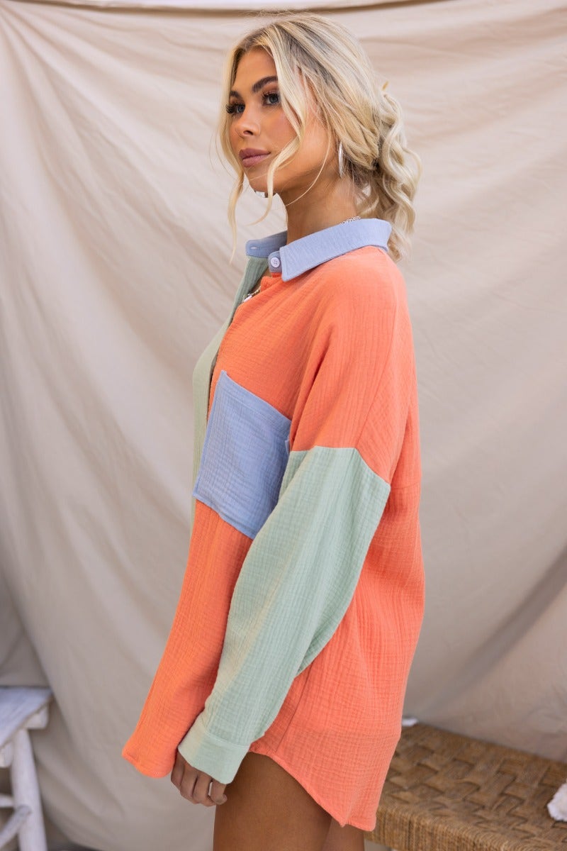 Model wearing the Atticus Top, a lightweight cotton button-up shirt in vibrant coral, blue, and green colors.