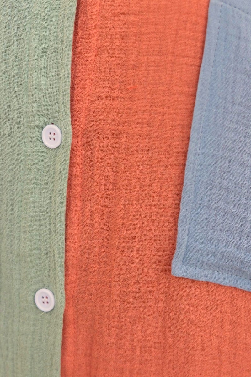 Close-up of Atticus Top showing textured cotton fabric in green, orange, and blue, featuring button-up front and pocket.